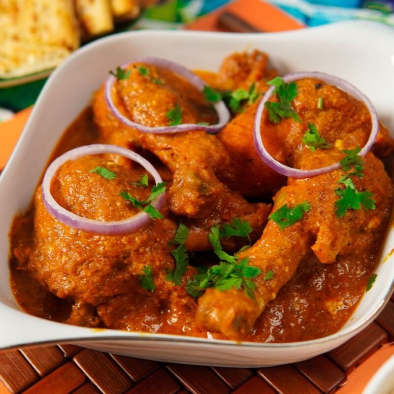 Naatu Kozhi Curry - spicy country chicken curry in thick reddish-brown gravy with onion and coriander garnish